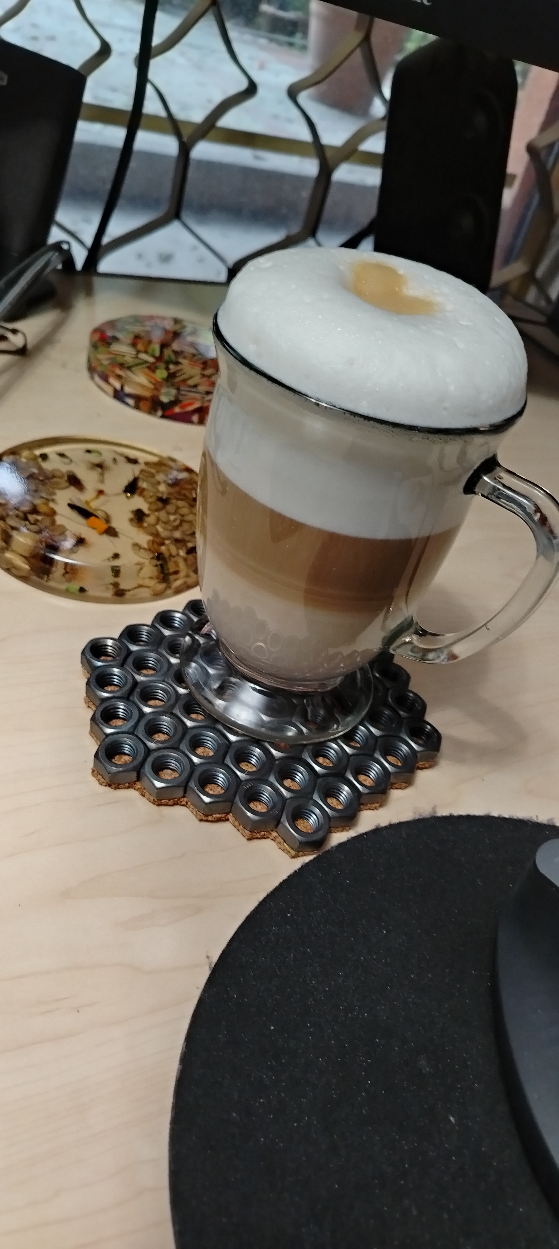 Coaster industrial de tuercas en acero natural sin pintar con café encima, sobre mesa de madera