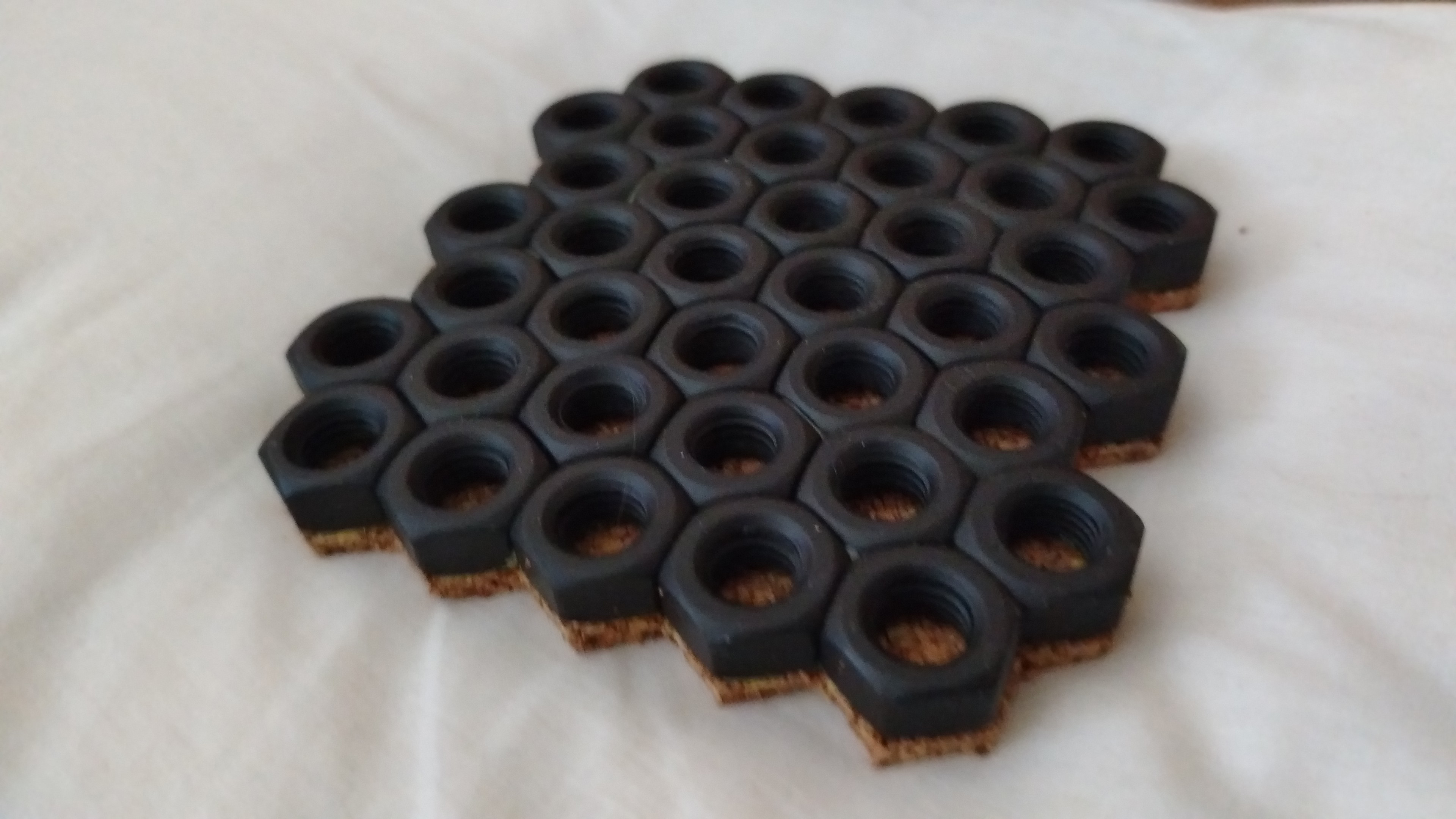 Set de coasters industriales formados por tuercas hexagonales soldadas, acabado negro mate con base de corcho